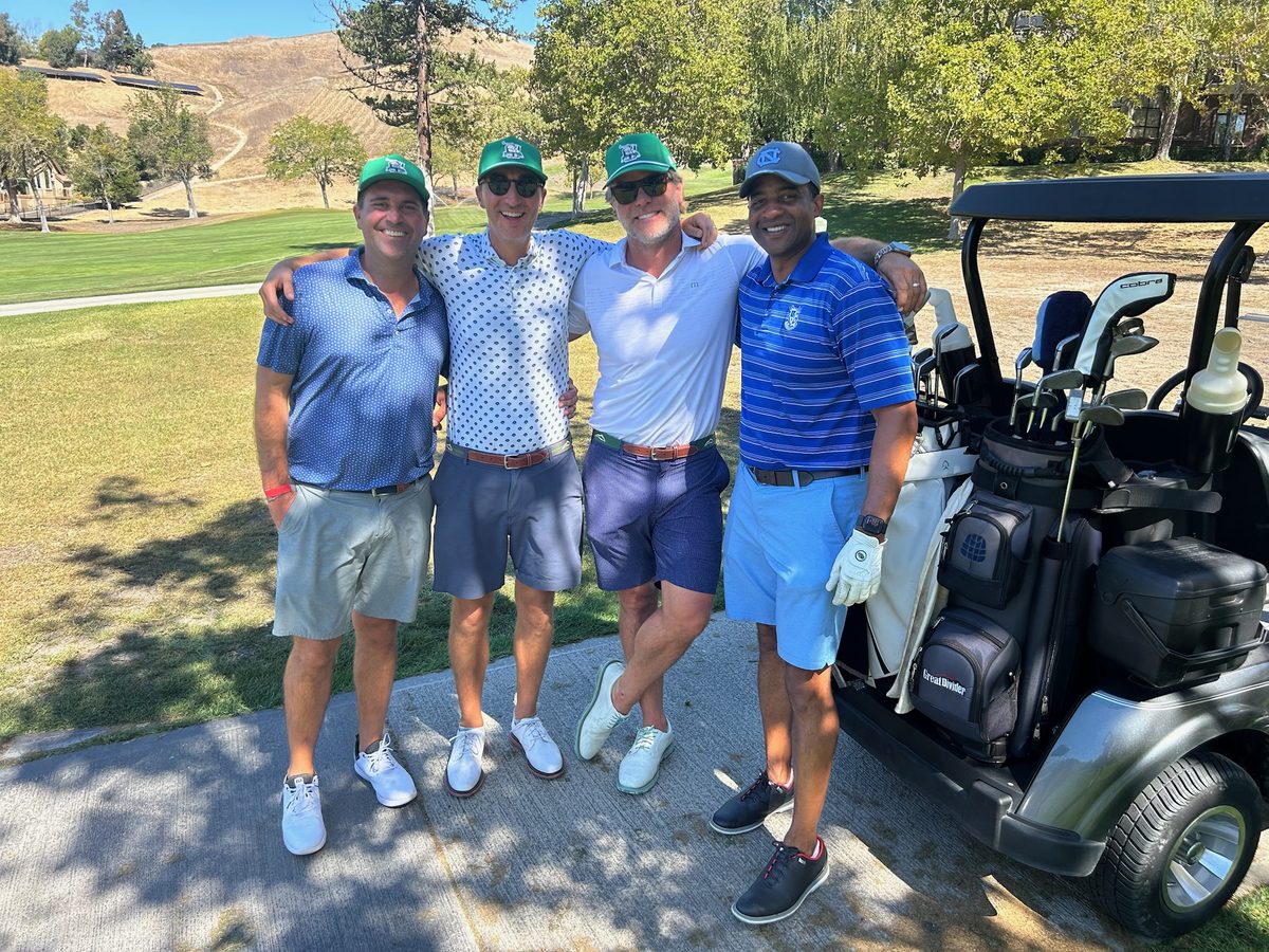 Foursome posing by the golf cart wearing matching green hats