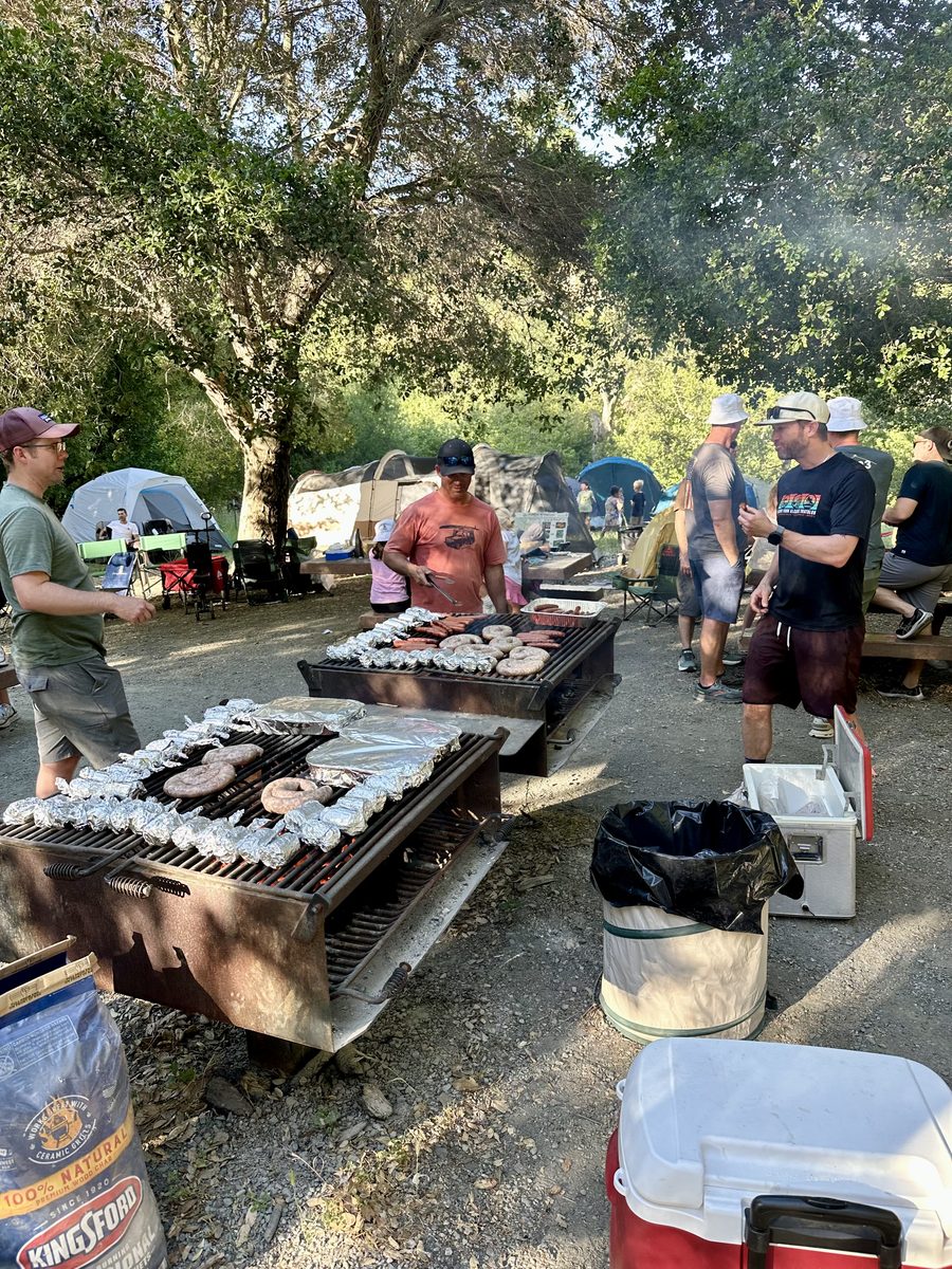 Dads grilling burgers at the campsite with tents in the background