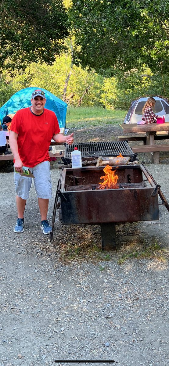 Dad starting the campfire with tents and picnic tables in the background