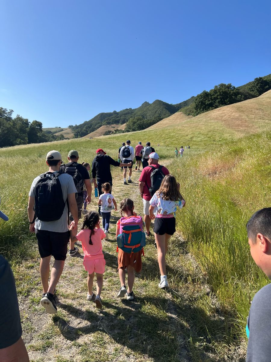Dads and kids hiking together on a trail through green hills